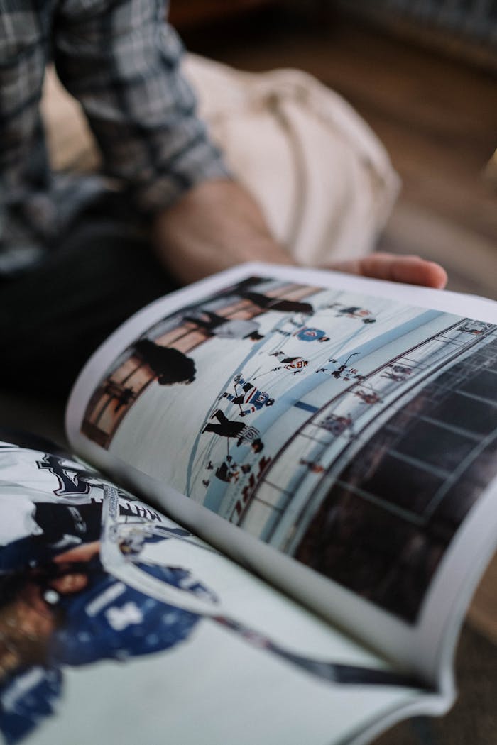 A close-up shot of a person reading a magazine with images of ice hockey scenes indoors.